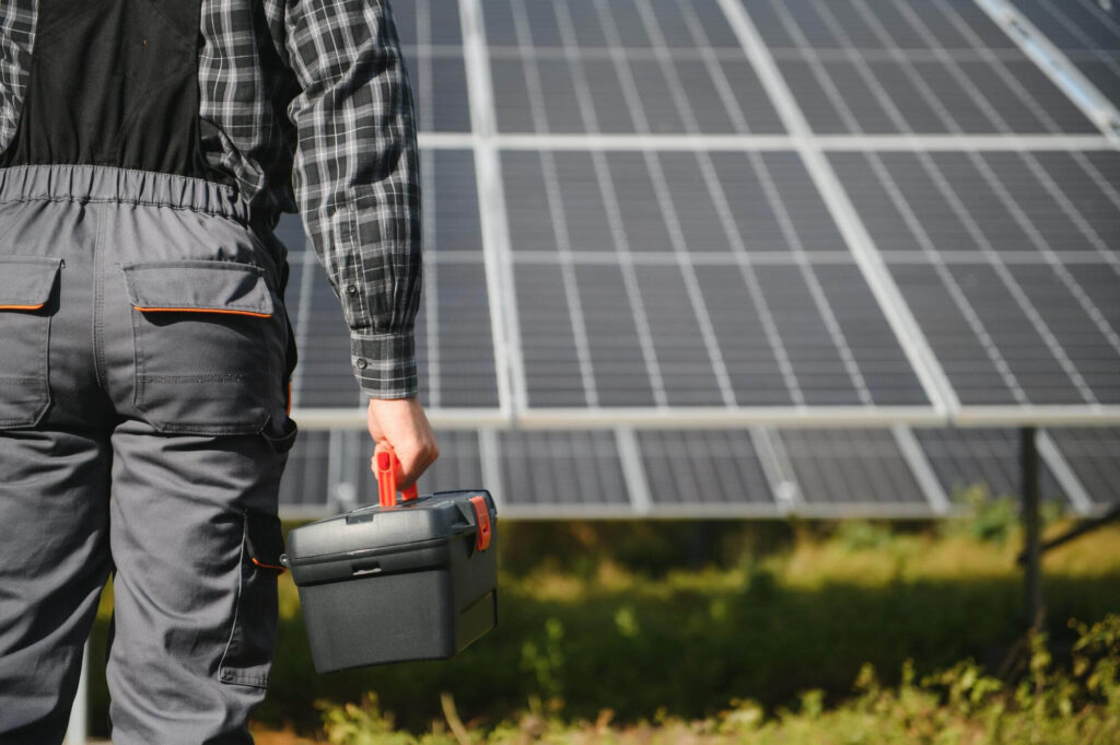 Uomo con una scatola di batterie in mano, posizionato di fronte a pannelli solari