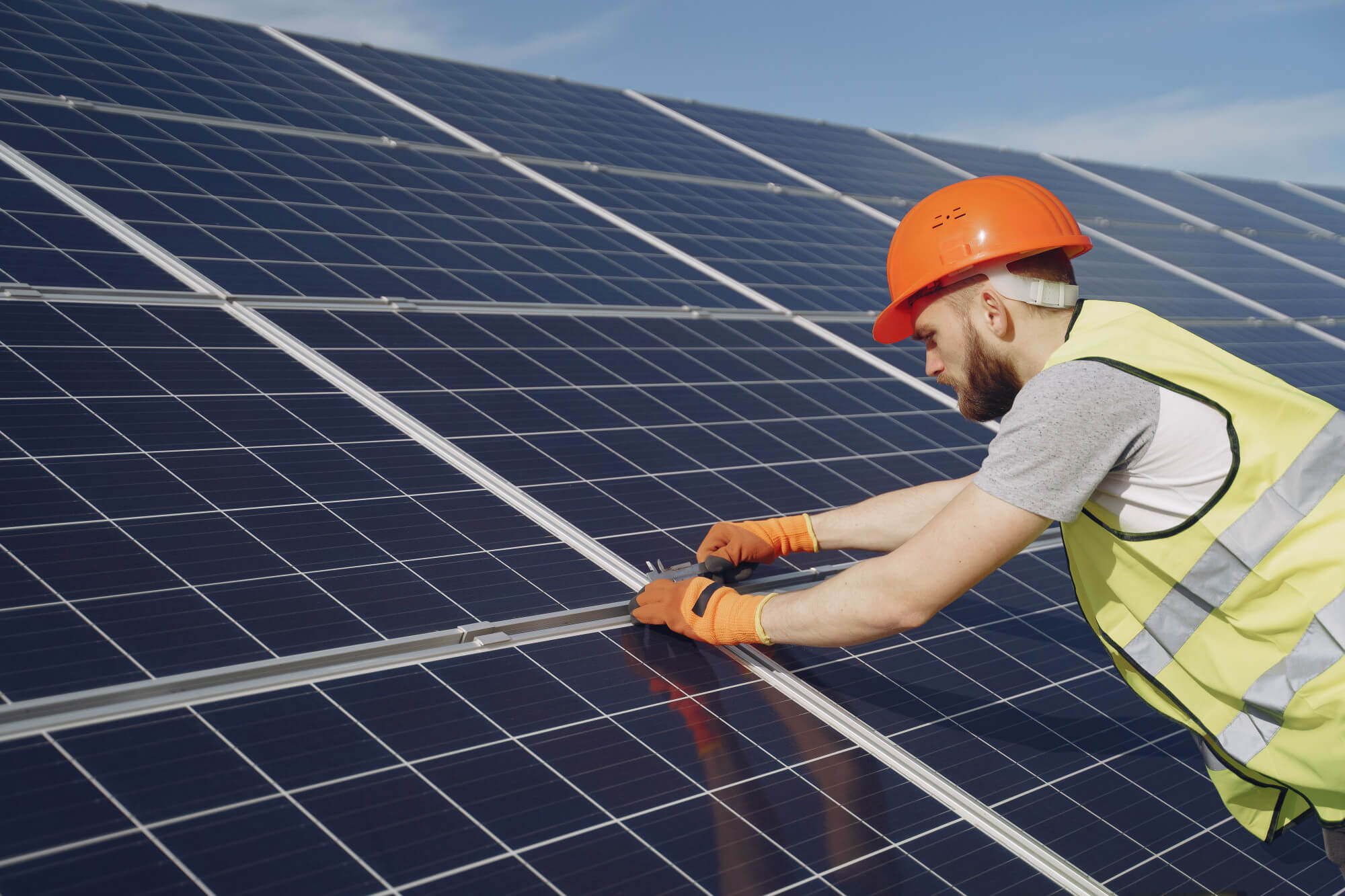 Lavoratore con casco arancione e giubbotto di sicurezza, mentre installa un pannello solare